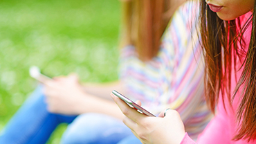 Tytöt selaavat kesäisellä nurmikolla matkapuhelinta.