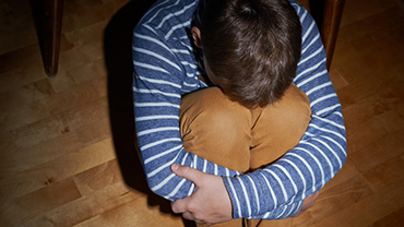 Poika istuu lattialla pää vasten polvia.