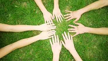 Lasten kädet nurmikolla muodostavat ympyrän.