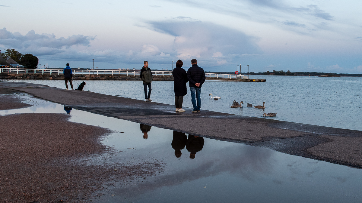 Ihmisiä silhuettina meren rannalla.