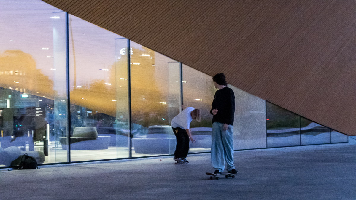 Kaksi nuorta poikaa skeittaa illalla Oodin edessä.