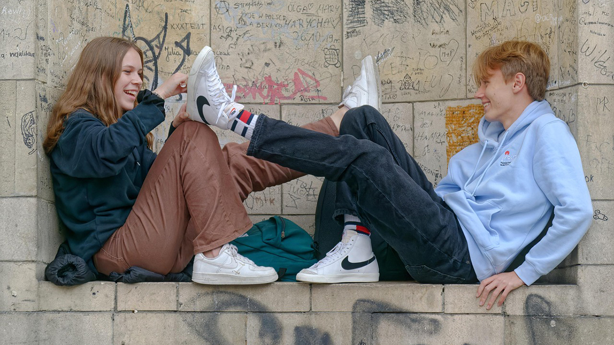 Tyttö ja poika istuvat graffitien peittämällä porrastasanteella.