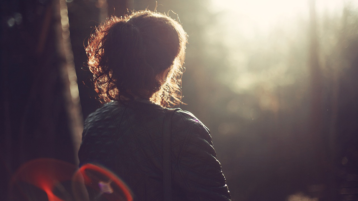 Nainen varjossa katsoo ikkunasta näkyvää valoa.